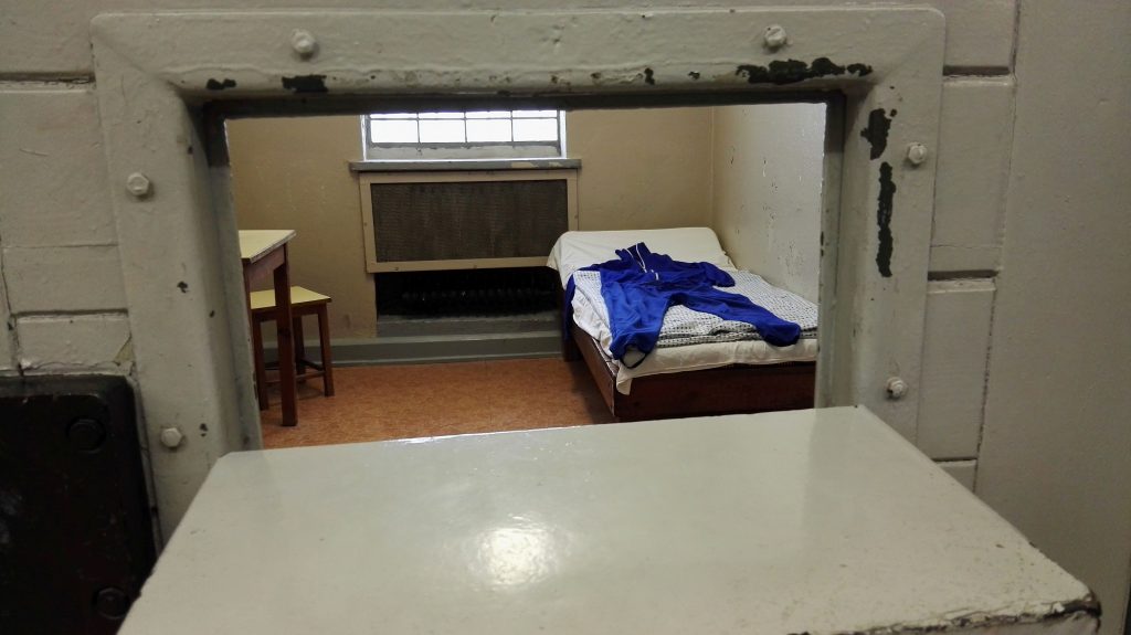 Blick durch die "Fressluke" in eine Zelle im Stasi-Gefängnis Berlin-Hohenschönhausen. Auf der Pritsche die Gefängniskleidung.